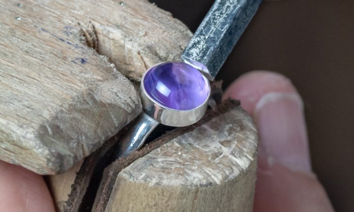 Tutor setting a cabochon stone with a pusher resting against jewellery bench peg
