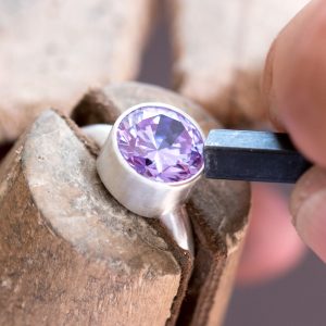 A large round faceted lavender cubic zirconia being set in a silver ring with a pusher tool