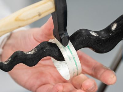 a silver bangle being hammered on an anticlastic raising stake against a plain grey background