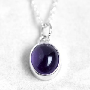 Silver pendant with amethyst cabochon gemstone on a silver chain against a stone background
